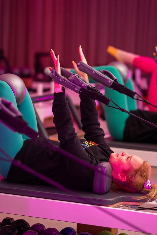 A Joyful Pilates member working on the reformer under colourful studio lighting