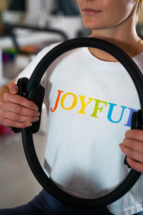 A member in a rainbow Joyful tee holding a Pilates ring